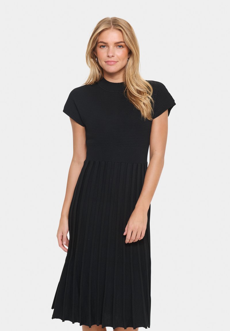 Black knit dress featuring a fitted top and pleated skirt, with short sleeves and a round neckline, creating a textured, flowing design.