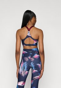 Sports-bh og leggins-sett med en mørkeblå bunn og rosa og blå abstrakte mønstre. Bh-en har en åpning på ryggen og brede stropper.