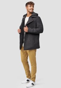Donkergrijze peacoat met een gestructureerde capuchon, dubbelgeknopte ontwerp, zijzakken, gecombineerd met kaki broek en witte sneakers.