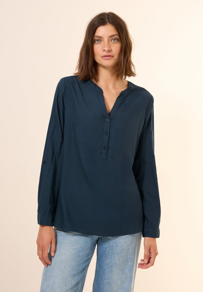Donkerblauwe lange mouwen shirt met een gedeeltelijke knoopsluiting en V-hals. Glad materiaal, ontspannen pasvorm en opgerolde mouwen met knooptab.
