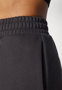 Pantaloni della tuta neri con vita elastica testurizzata, tessuto liscio e dettagli di pieghe laterali sottili, offrono una vestibilità comoda e rilassata.