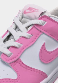 Baskets Nike blanches et roses avec des lacets blancs, un swoosh Nike rose visible et un logo Nike rose sur la languette.