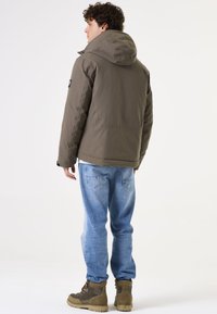 Chaqueta con capucha marrón, cierre de cremallera, diseño acolchado. Combinada con jeans azul claro y botas marrones. Estilo minimalista, textura suave, logotipos sutiles.