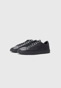 Schwarze Sneakers aus einer Mischung aus glattem und strukturiertem Leder, mit subtilen geometrischen Mustern und einer flachen Gummisohle. Verstellbare Schnürsenkel.