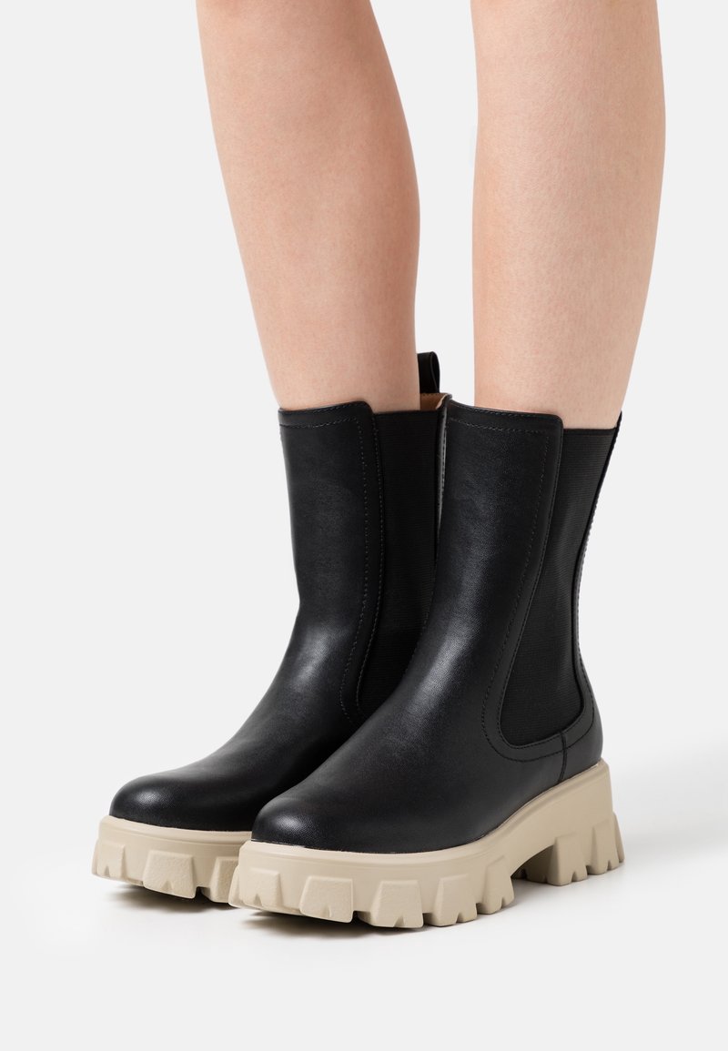 Botines de cuero negro con paneles laterales elásticos y suelas de goma beige gruesas con borde dentado. Acabado liso, detalles de costura mínimos.
