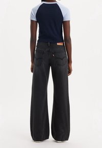 Czarne dżinsy o szerokich nogawkach z wysokim stanem, wyposażone w tylne kieszenie i czerwoną metkę. Połączone z granatowym i jasnoniebieskim topem z rękawami raglan.