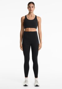 Crni sportski crop top i tajice visokog struka, prilagođenog dizajna, glatke teksture, minimalni šavovi. Model nosi bijele tenisice.