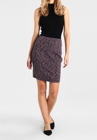 Haut sans manches noir côtelé associé à une jupe crayon à motif de longueur genou avec un design en zigzag bordeaux, blanc et bleu. Chaussures plates noires.