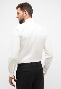 Witte lange mouwen shirt met een strakke kraag en knopped cuffs, gecombineerd met zwarte op maat gemaakte broeken met achterzakken en strakke naden.