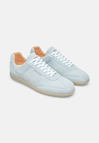 Sneakers in camoscio blu chiaro con una texture liscia, lacci bianchi, interno beige e suola in gomma beige. Marchio "Henry Stevens" visibile.