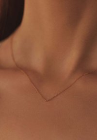 Gouden, delicate ketting met een eenvoudige V-vormige ontwer, rustend op gladde huid, waar het de fijne textuur en minimalistische stijl benadrukt.