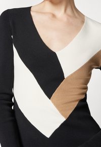 Maglione lavorato a maglia con scollatura a V, caratterizzato da blocchi di colore nero, bianco e marrone chiaro disposti in un motivo diagonale. Texture liscia, maniche lunghe.
