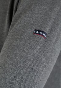 Grå strikket trøje med en blød tekstur, prydet med et lille sort og rødt "Armor Lux" mærke på ærmet. Enkel og klassisk design.