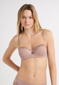 Reggiseno in morbido tessuto color nudo con finitura liscia, coppe sagomate e spalline sottili regolabili, con dettagli in mesh al centro.