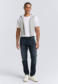 Valge T-särk, hall kampsun õlgade kohal, tumedad teksad ja valged tossud. Rõhk juhuslikul, kihilisel välimusel ja teksariide tekstuuril.