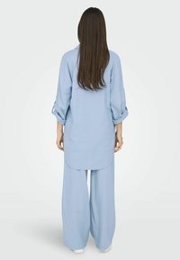 Tunique bleu clair à manches longues, au fit ample et à l'ourlet arrondi, associée à un pantalon large assorti. Textile lisse et silhouette décontractée.