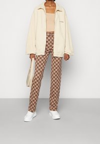 Krémová manšestrová bunda, béžový zkrácený top, hnědo-krémové kostkované kalhoty a bílé tenisky. Malá kabelka přes rameno.