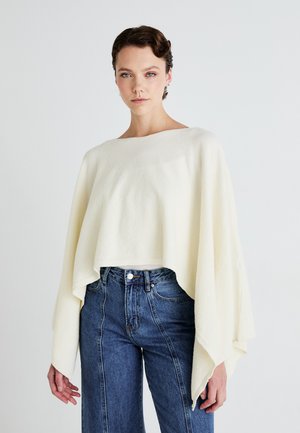 Witte cropped pullover met een brede halslijn en vloeiende mouwen, gemaakt van zachte textuurstof, gecombineerd met high-waisted blauwe denim jeans.