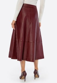 Middenlange bordeauxrode leren rok met een uitlopende silhouet, gladde textuur en een naaddetail. Gecombineerd met bijpassende hoge hakken.