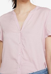 Blouse rose à manches courtes avec un col en V, dotée d'un devant boutonné et d'un imprimé à pois blancs sur un tissu doux. Design décontracté avec une coupe ample.