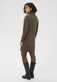 Robe en tricot marron avec col haut, ourlet côtelé et manches longues, associée à des bottes noires montantes.