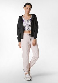 Sudadera con capucha negra, top recortado multicolor con patrón morado, pantalones de chándal rosa claro y zapatillas grises con acentos blancos.