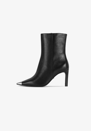 Schwarzer Leder-Stiefelette mit spitzer Metallkappe und schmalem hohen Absatz, seitlich auf weißem Hintergrund gesehen.