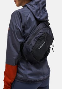 Zaino nero con forma curvata, realizzato in tessuto leggero; presenta spallacci regolabili, logo e dettagli in rete.