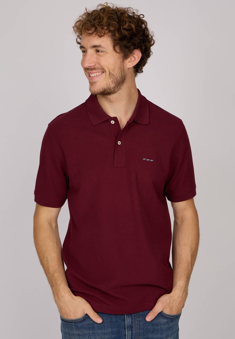 Polo shirt bordeaux en coton, avec un col, une patte de boutonnage à deux boutons et un petit logo brodé sur la poitrine. Manches courtes.