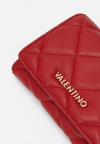 Portofel din piele matlasată roșie, cu brandul "VALENTINO" în nuanță aurie. Designul include cusături distincte și o textură netedă.