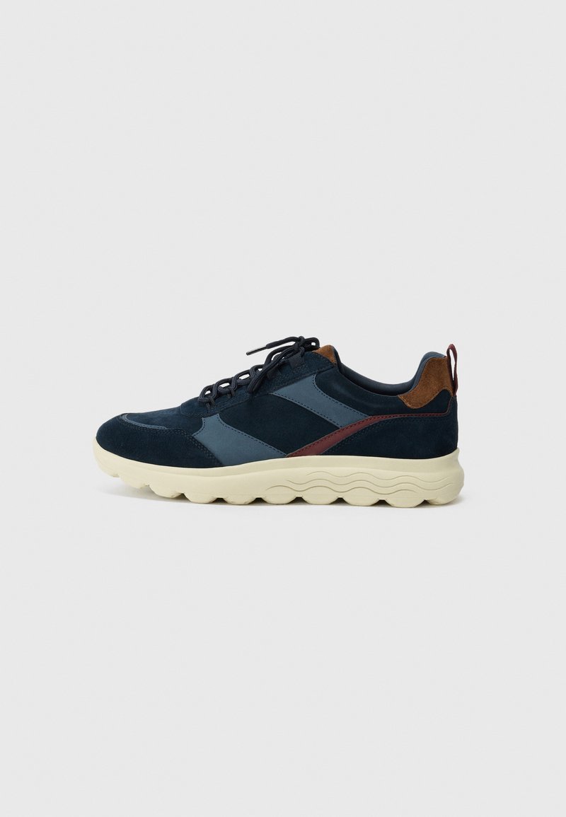 Navy and dark blue suede sneaker with a beige textured sole, featuring brown leather accents and black laces. Side panel design detail.