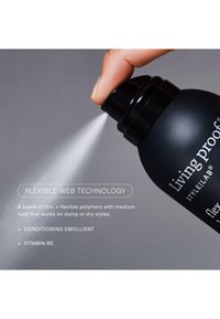 Main appuie sur la buse du spray d'une bouteille noire de produit capillaire Living Proof, libérant une fine brume sur fond gris.
