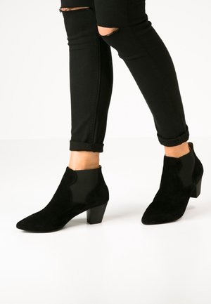 Zwarte suède enkellaarzen met een spitse neus, elastische zijkanten en een chunky hak. Draagt met zwarte jeans, voorzien van een omslag en versleten details.