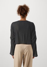 Pull en tricot noir à côtes avec un design court et des manches longues, présentant une texture subtile et des détails de points ouverts à l'arrière.