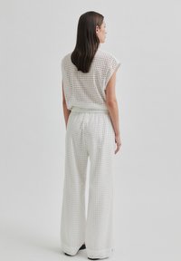 Bílý, strukturou texturovaný dvoudílný outfit obsahující volný, krátký top s širokými rukávy a kalhoty s vysokým pasem a širokými nohavicemi s vzorovaným designem.