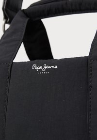 Juodas šoninis krepšys, pasiūtas iš tekstūruotos medžiagos su matomomis siūlėmis. Logotipas "Pepe Jeans London" siuvinėtas priekyje.