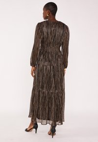 Robe maxi plissée noire et dorée avec manches longues, taille élastique et design à volants. Fini avec un ourlet fluide et une texture douce.