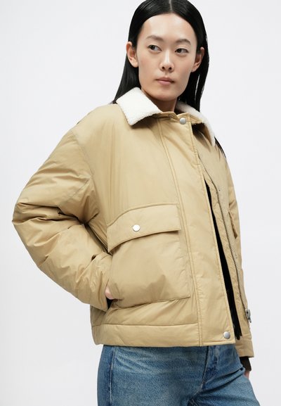 Beež värviga paks jakk kunstkarusnahast kraega, ees klõpsuga sulgumise ja küljetaskutega. Omaduseks lühendatud lõige ja tugev kangas.