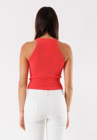 Top in morbido tessuto rosso a costine con un design aderente e collo alto, abbinato a jeans in denim bianco, visto da dietro, mettendo in evidenza il taglio sulle spalle.