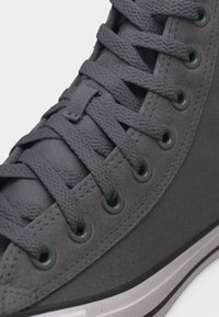 Κοντινό πλάνο κορδονιών γκρι αθλητικού παπουτσιού διαπερασμένων από τρύπες στο ύφασμα και την επάνω σουέτ επιφάνεια με ορατές ραφές και μέρος της λευκής καουτσούκ σόλας.