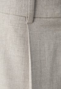 Tissu en lin beige présentant une texture lisse avec un motif de tissage subtil et une couture verticale sur le côté.