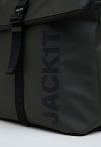 Grön vattentät väska med svarta accenter, med en iögonfallande logotyp "JACK1T". Slät textur, robust rem och design med klaffstängning.
