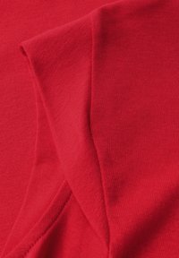 Tissu en coton rouge montrant une texture lisse avec des détails nervurés. Le matériau est léger et plié, révélant sa couleur vibrante.