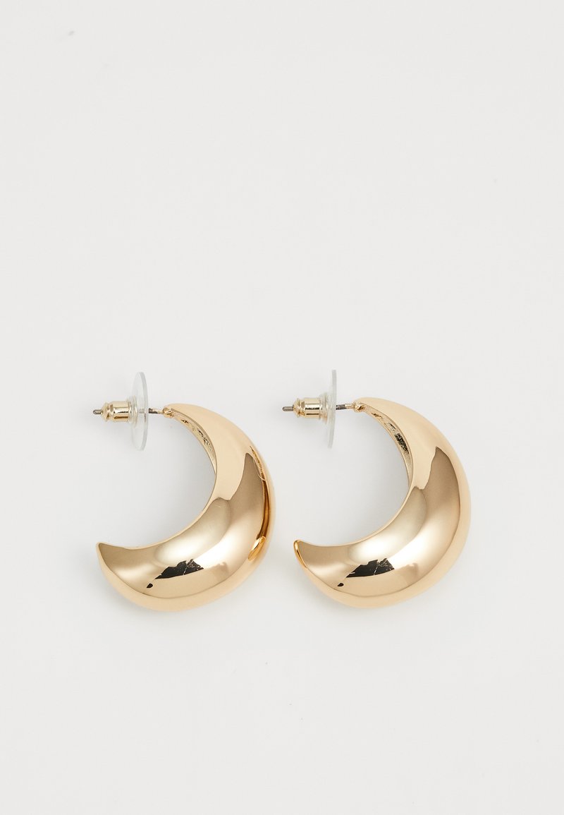 Gold-colored metal earrings in a crescent shape, featuring a polished surface, stud backing, and transparent silicone stoppers.