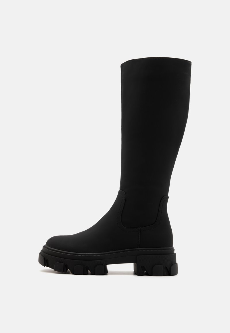 Botte noire montant jusqu'au genou avec semelle crantée épaisse et dessus lisse, montrée de profil sur fond blanc.