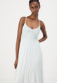 Gaiši zils, grīdā garš kleita ar adītu augšu un mežģīņu akcentu viduklī, ar plānām siksnām un plūstošu teksturētu svārku.