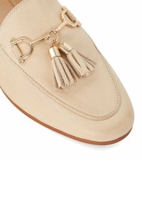 Beige leren instappers met een gladde textuur, spitse neus en een metalen siersluiting met twee franjes en gouden accenten.
