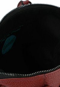 Sac à main en cuir rouge avec une ouverture à glissière, présentant une doublure intérieure noire et une texture subtile. Logo visible à l'intérieur.