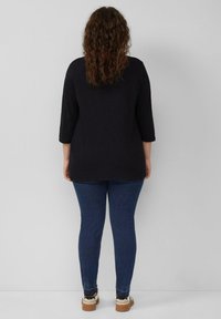 Zwarte lange mouwen top gecombineerd met blauwe skinny jeans en beige sneakers. De top heeft een losse pasvorm, terwijl de jeans aansluitend zijn met subtiele stiksels.