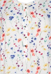 Blumenbluse aus leichtem Stoff mit weißem Hintergrund, mehrfarbigen Blumenmustern und dekorativen Knöpfen auf der Vorderseite.